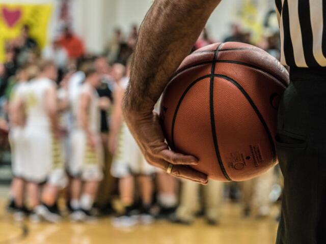 Basketball official holding the basketball during a team huddle.