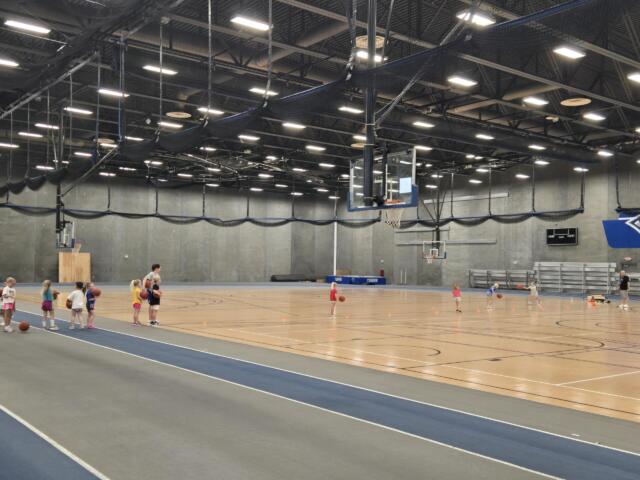 Kids and coaches in a gym for a basketball camp doing a drill