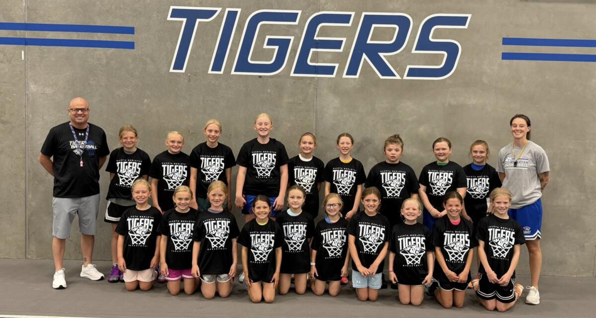 Group of young basketball players in black Tigers shirts posing for a team photo in a gym period great wall background with TIGERS lettering behind them