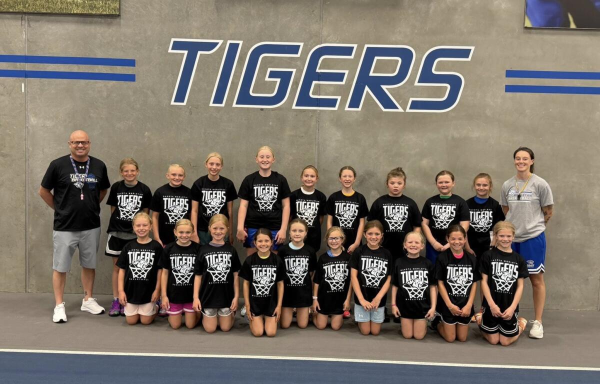 Group of young basketball players in black Tigers shirts posing for a team photo in a gym period great wall background with TIGERS lettering behind them