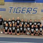 Group of young basketball players in black Tigers shirts posing for a team photo in a gym period great wall background with TIGERS lettering behind them