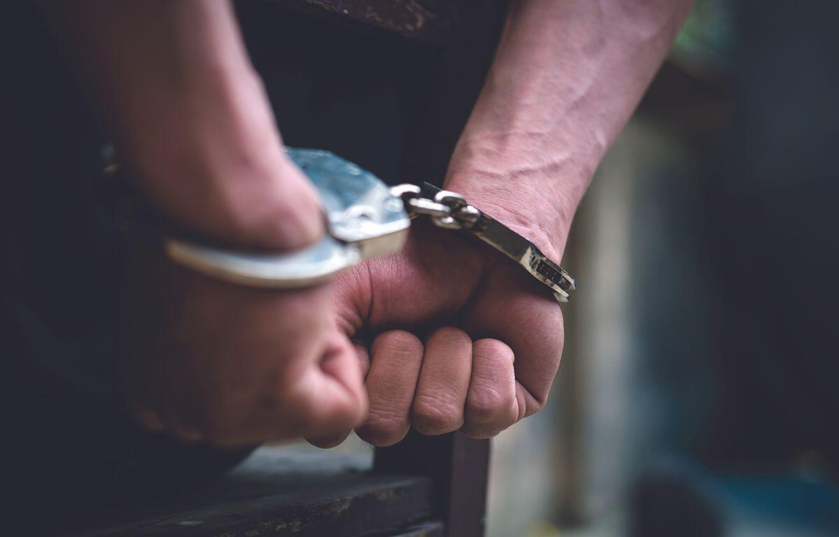 Close-up of hands in metal handcuffs, wrists bound and resting on a surface.