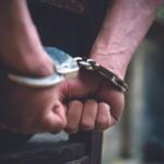 Close-up of hands in metal handcuffs, wrists bound and resting on a surface.