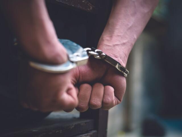 Close-up of hands in metal handcuffs, wrists bound and resting on a surface.