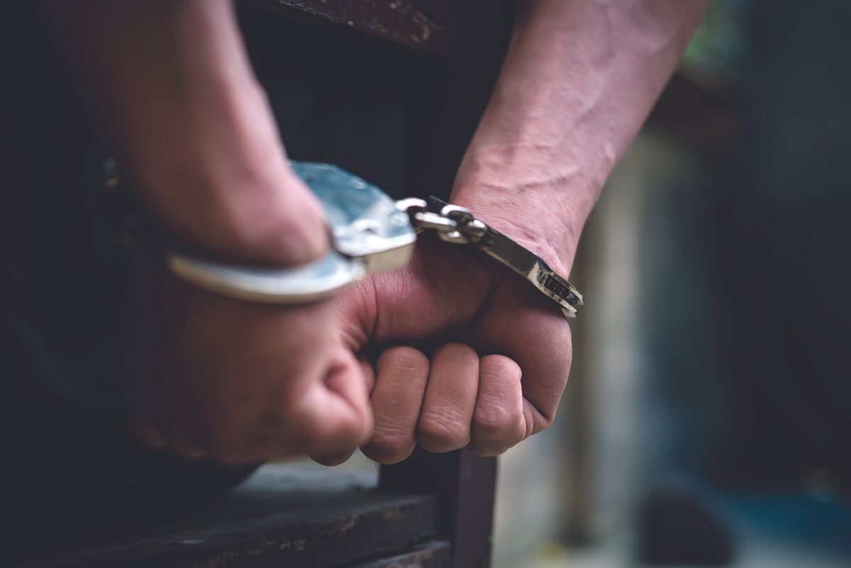 Close-up of hands in metal handcuffs, wrists bound and resting on a surface.