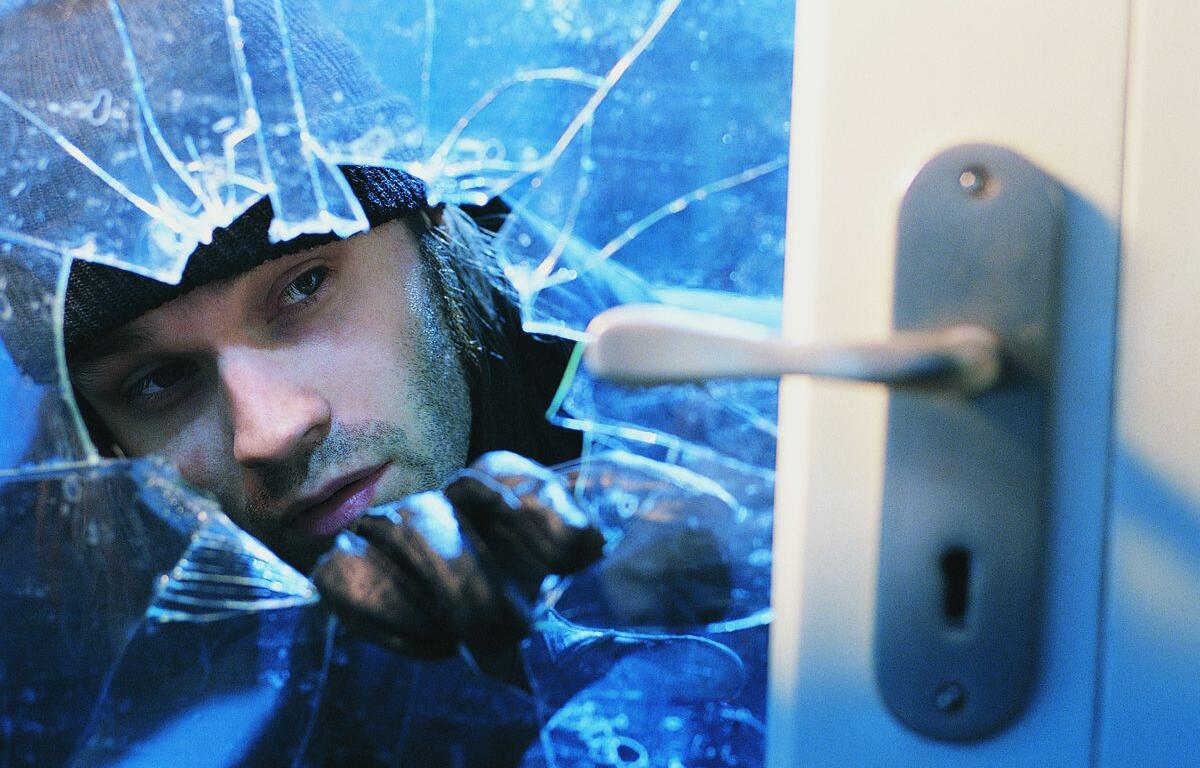 Burglar breaking the glass on a door.