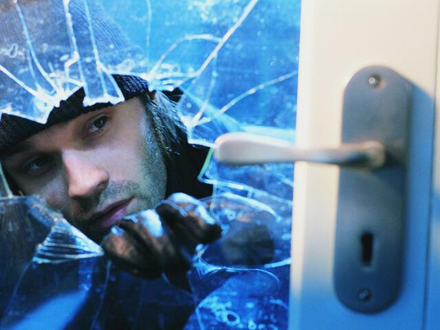 Burglar breaking the glass on a door.