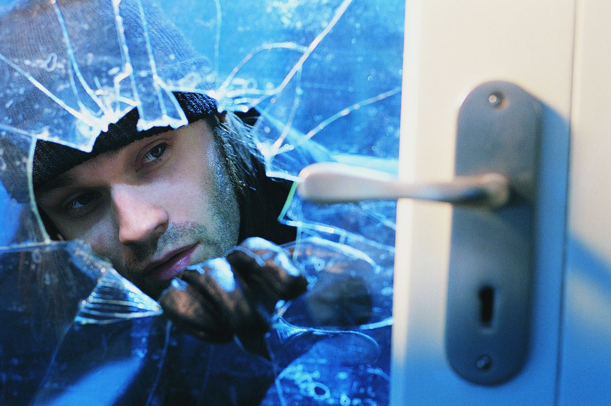 Burglar breaking the glass on a door.