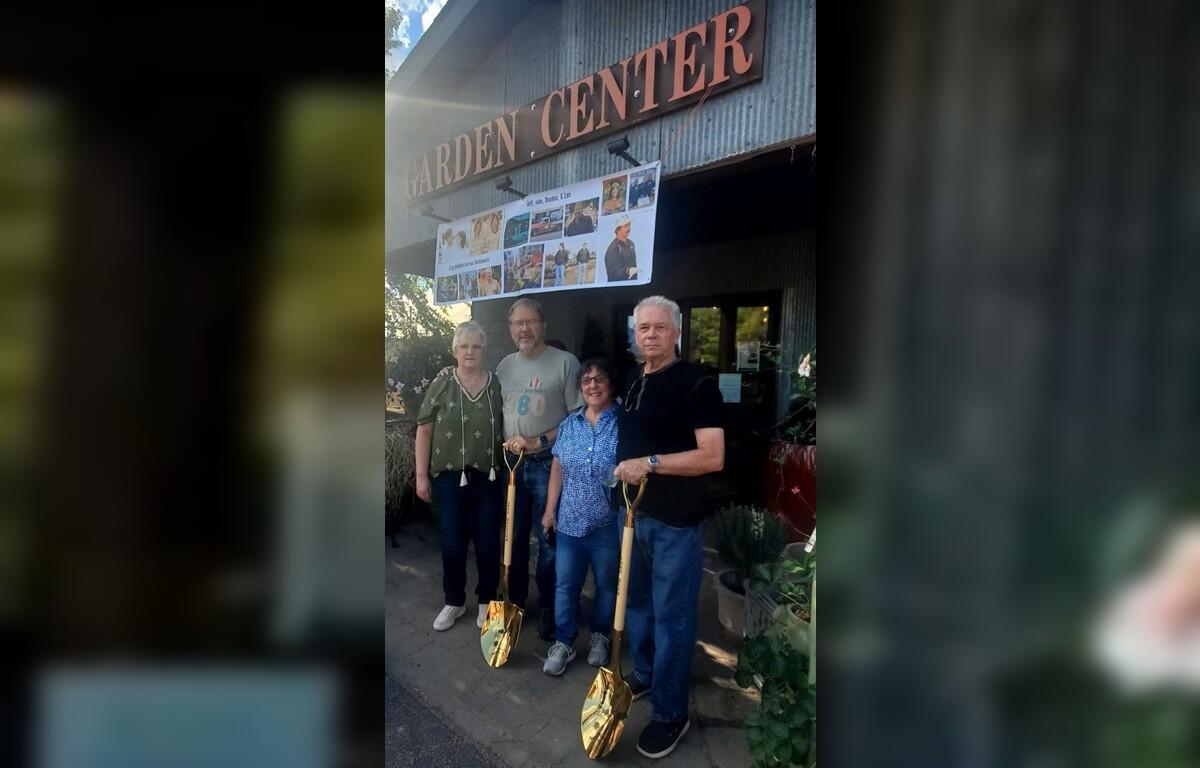 Four adults pose outside a garden center entrance, each holding a gold-colored shovel with a banner of photos above them.