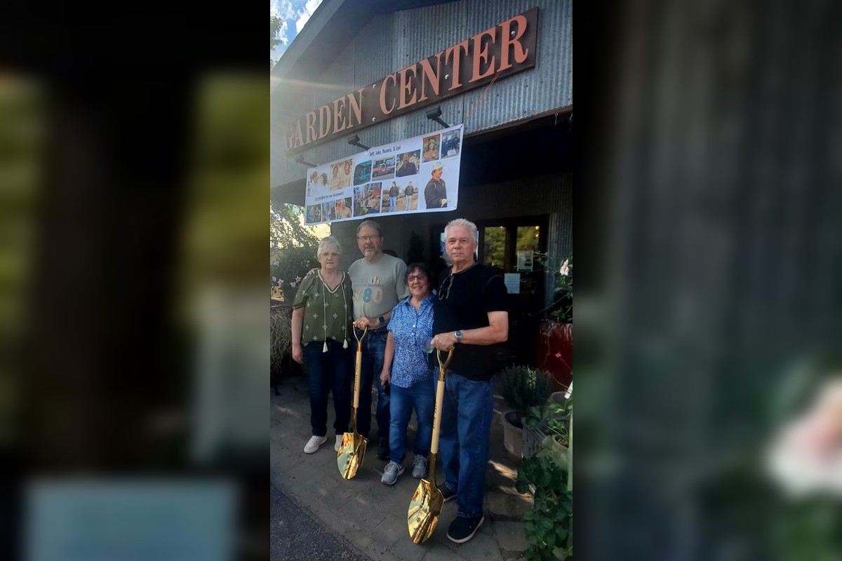 Four adults pose outside a garden center entrance, each holding a gold-colored shovel with a banner of photos above them.