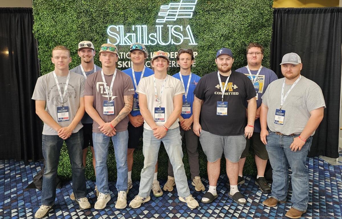 Group of nine men posing for a photo at a SkillUSA event, wearing lanyards and badges in front of a greenscreen backdrop with SkillUSA logo.