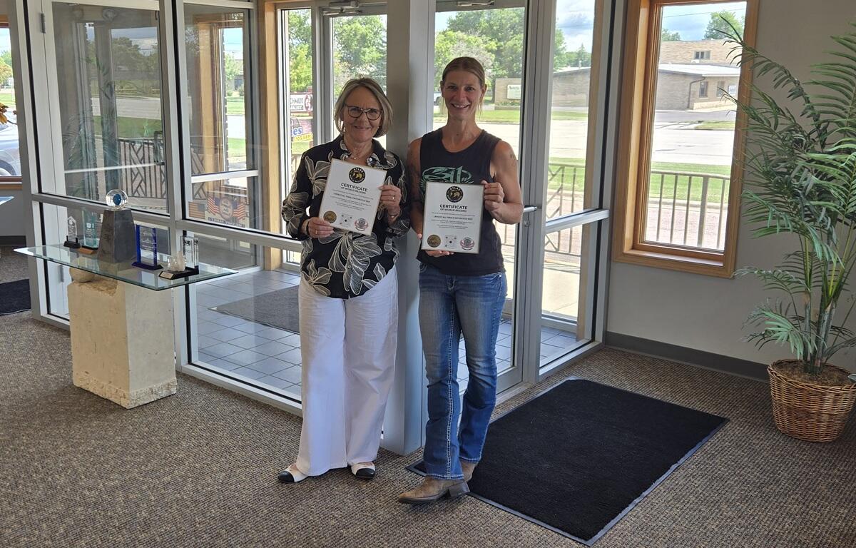 Two women stand in a lobby holding certificates, smiling at the camera.