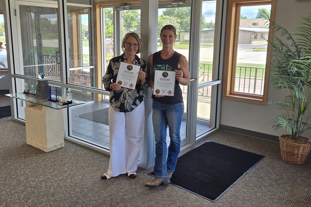 Two women stand in a lobby holding certificates, smiling at the camera.