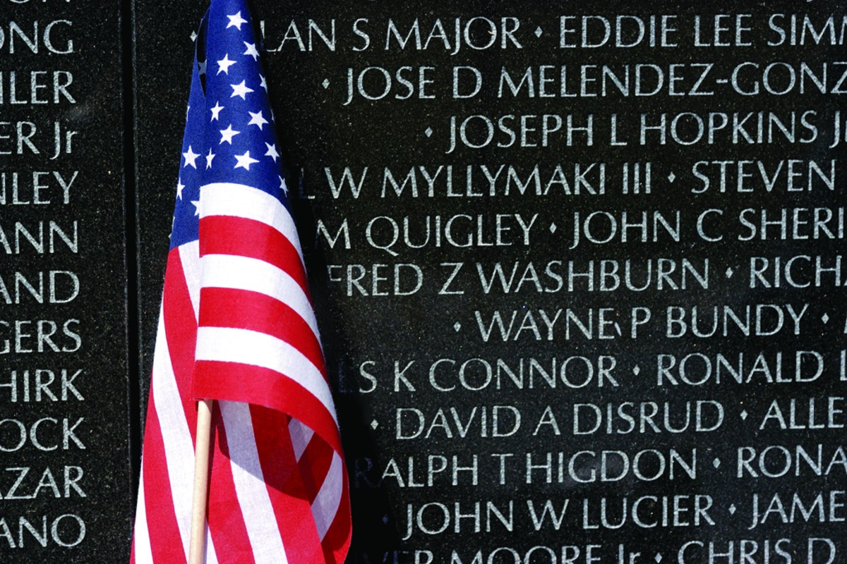 American flag draped in front of a memorial wall engraved with names on dark granite surface, commemorating the fallen.