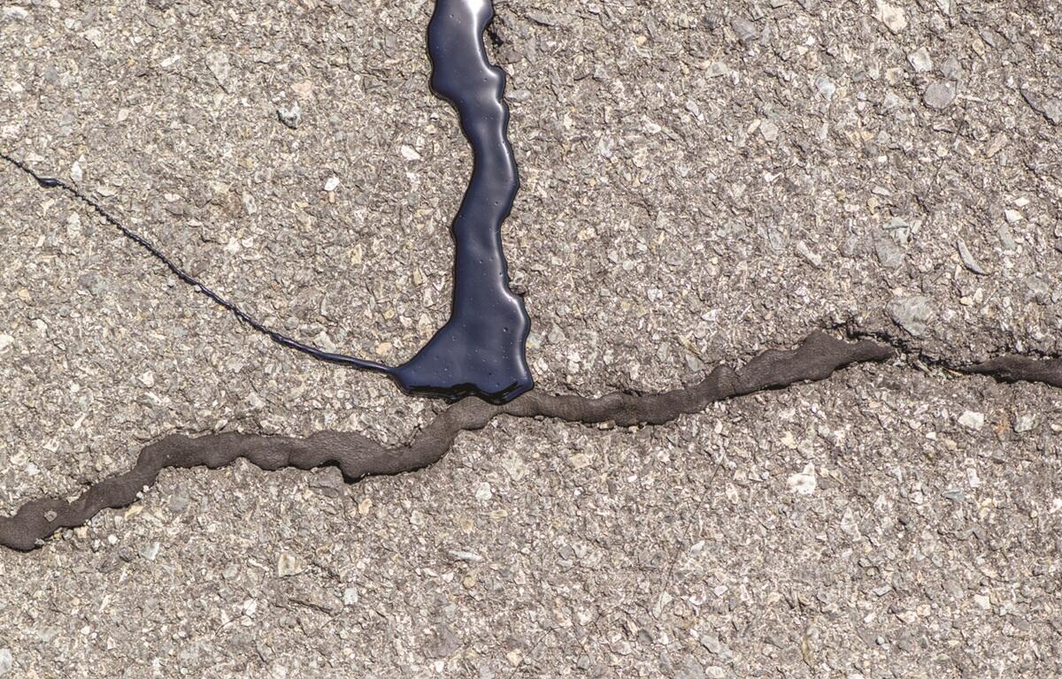 Crack in asphalt filled with dark sealant along the seam